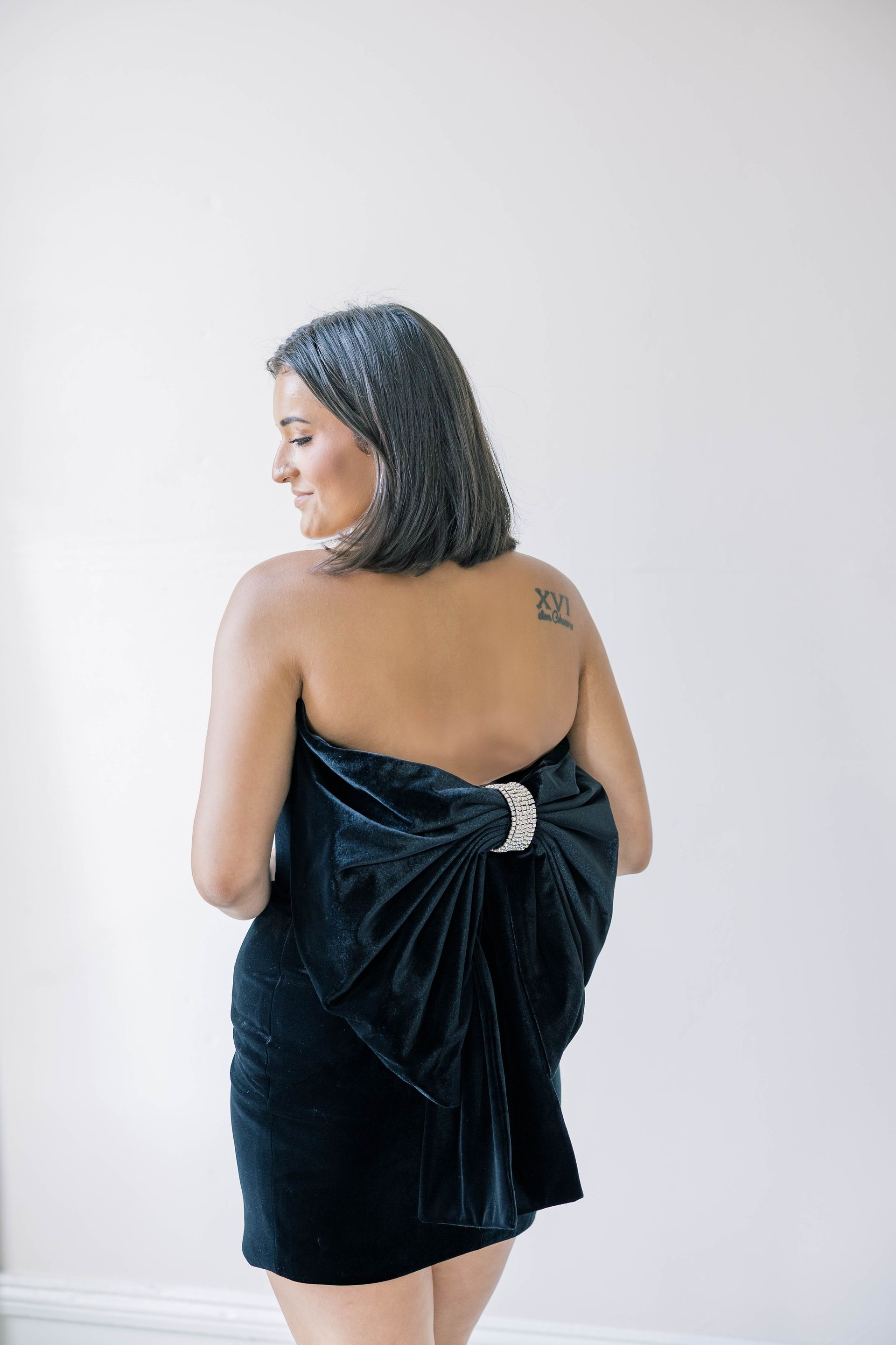 A woman in a black dress is standing in front of a white wall.
