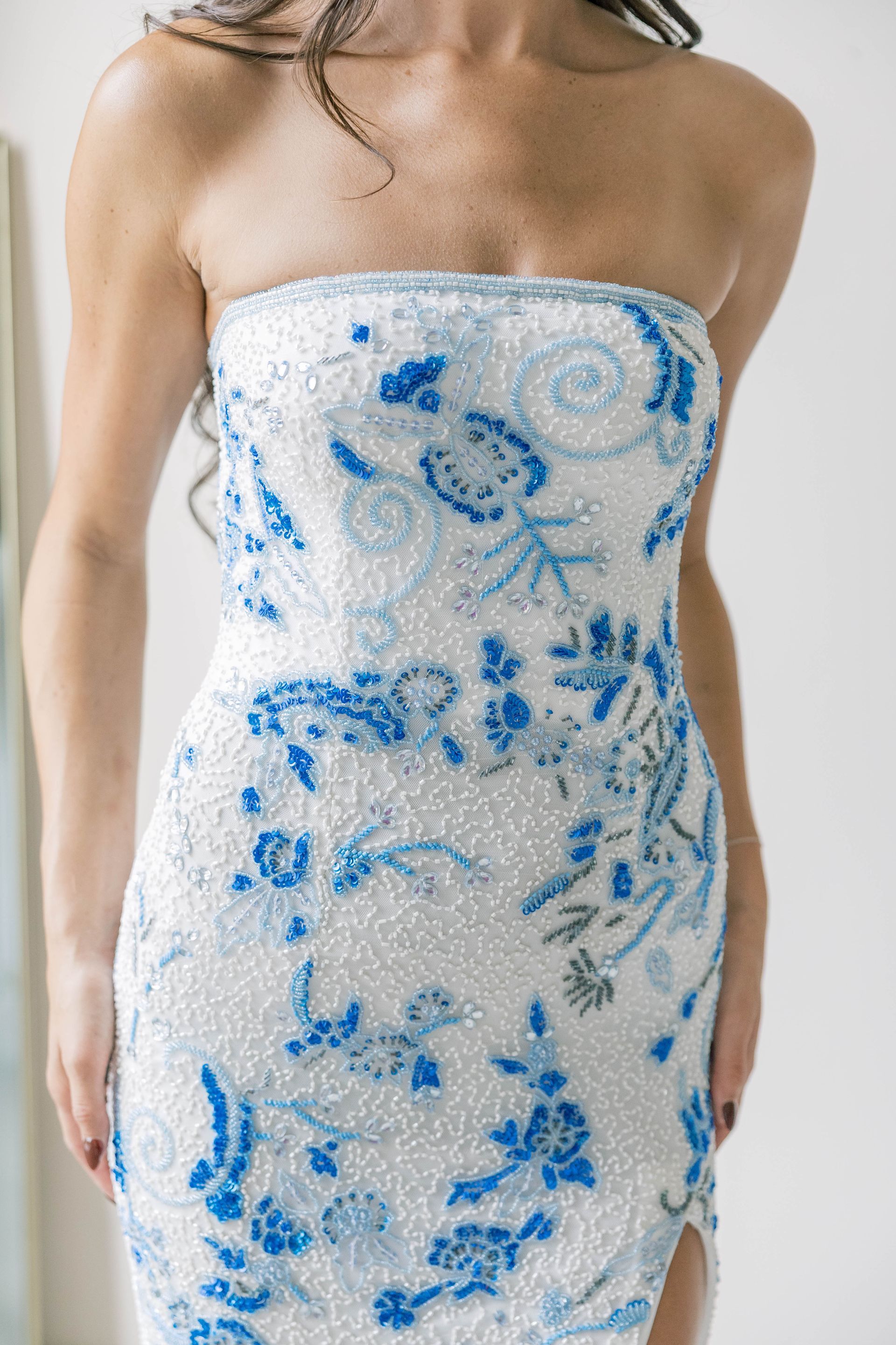 A woman in a purple sequined dress is standing in front of a white wall.