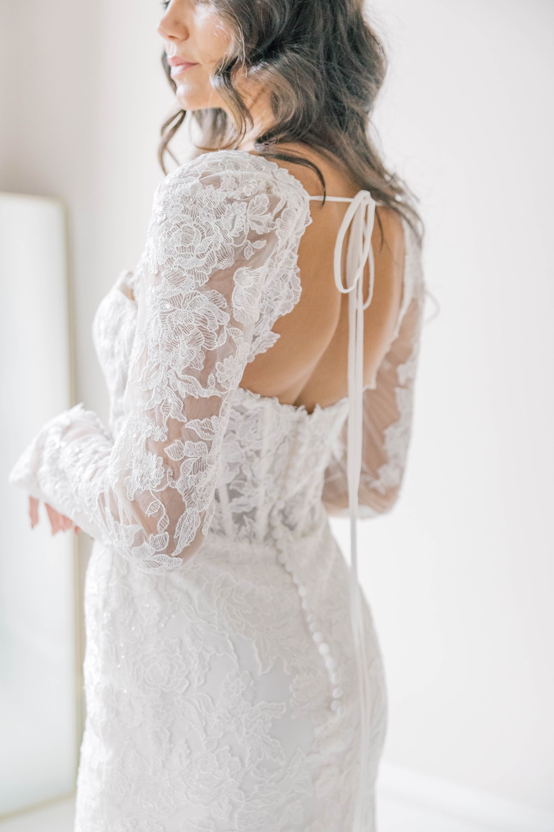 Woman in white lace wedding dress, back view, tie detail, long sleeves.