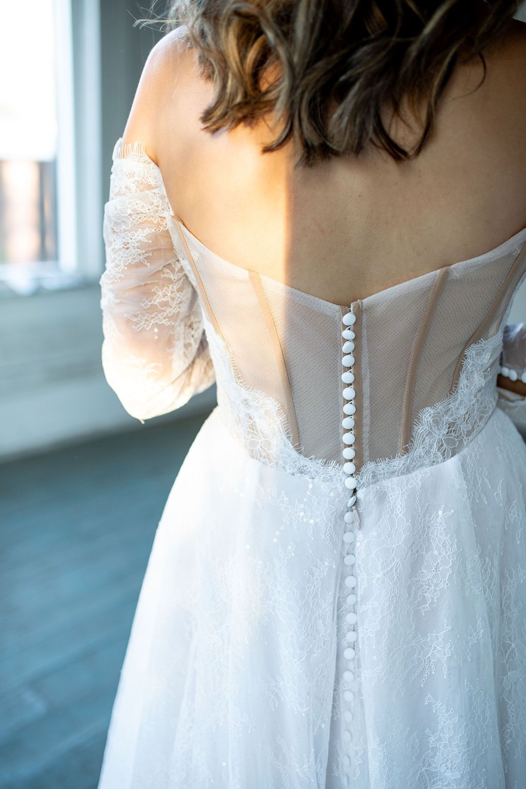 A woman in a wedding dress is standing in front of a window.