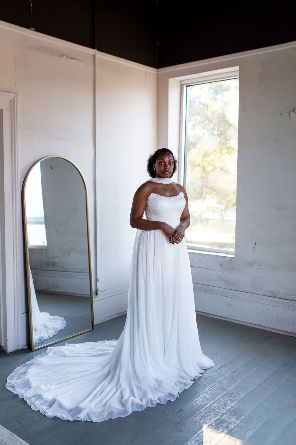 A woman in a wedding dress is standing in front of a mirror in a room.
