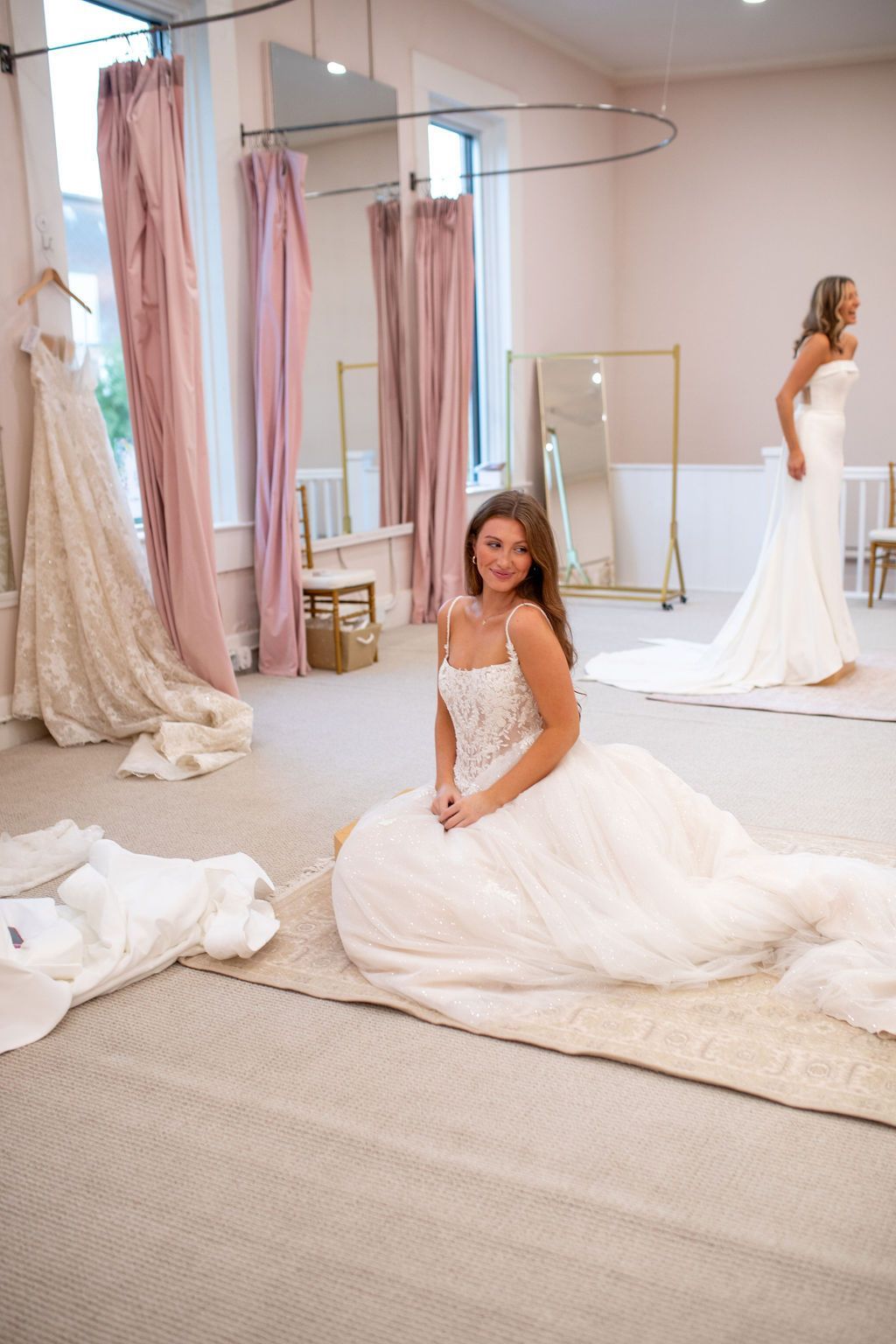 A woman in a wedding dress is sitting on the floor in a dressing room.