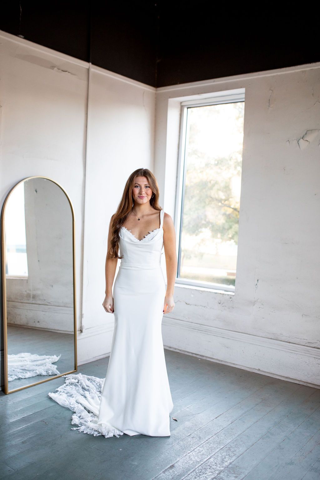 A woman in a white wedding dress is standing in front of a mirror in a room.