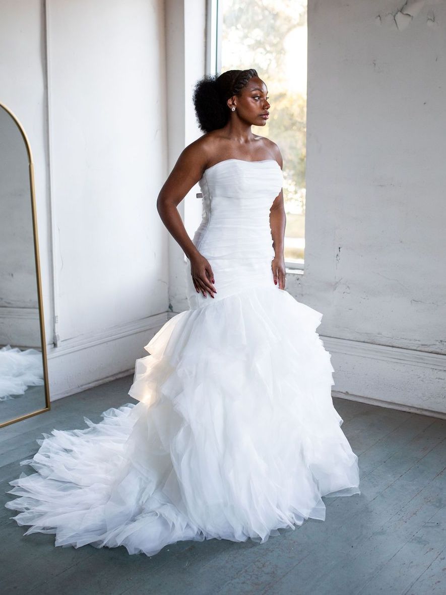 A woman in a white wedding dress is standing in front of a mirror.