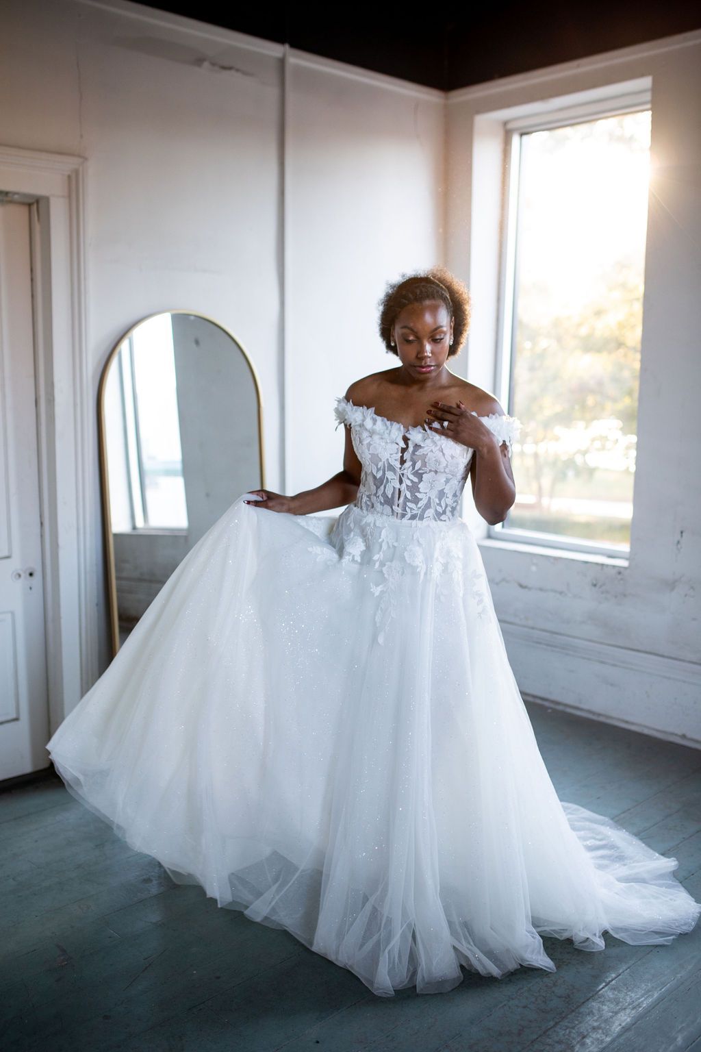 A woman in a wedding dress is standing in front of a mirror in a room.