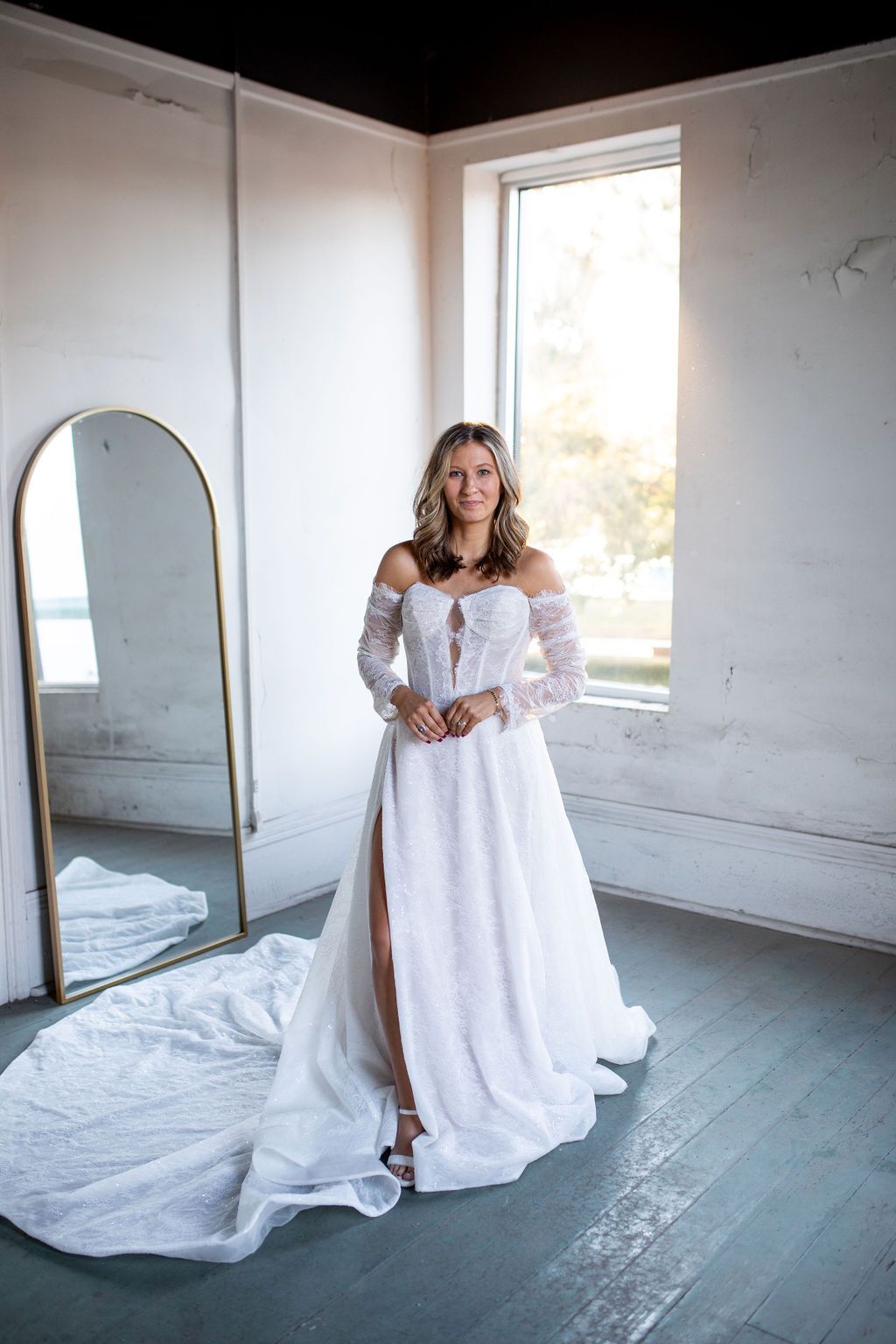 A woman in a white wedding dress is standing in front of a mirror.