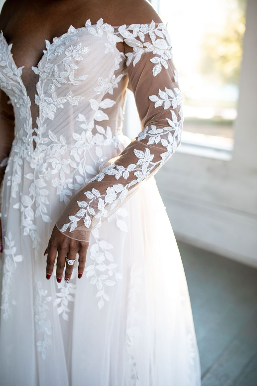 A woman is wearing a white lace wedding dress with long sleeves.