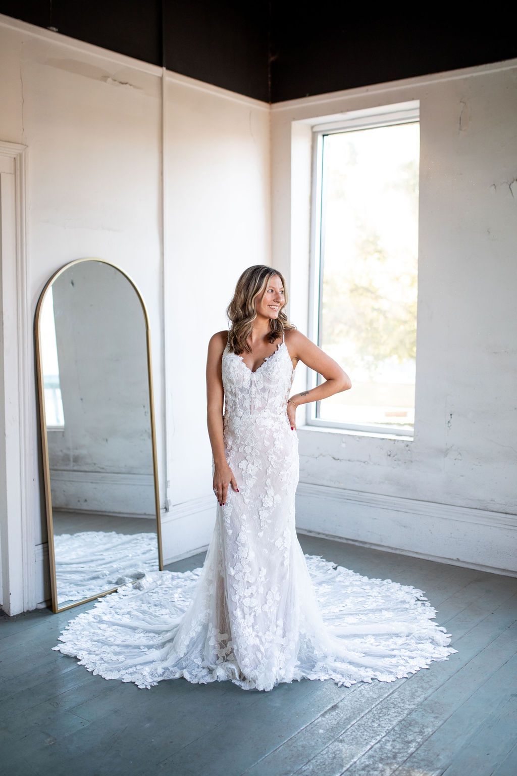 A woman in a wedding dress is standing in front of a mirror in a room.