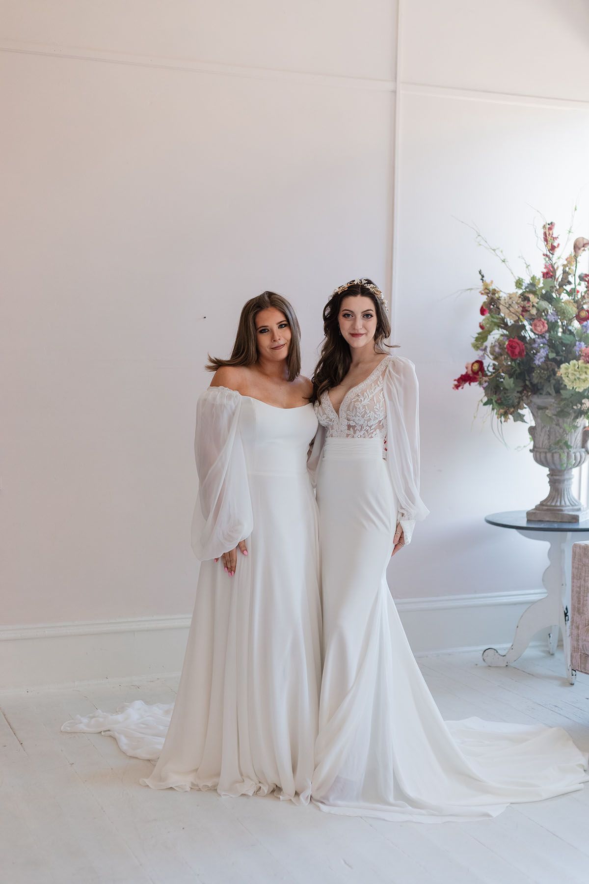 Two women in wedding dresses are standing next to each other in a room.