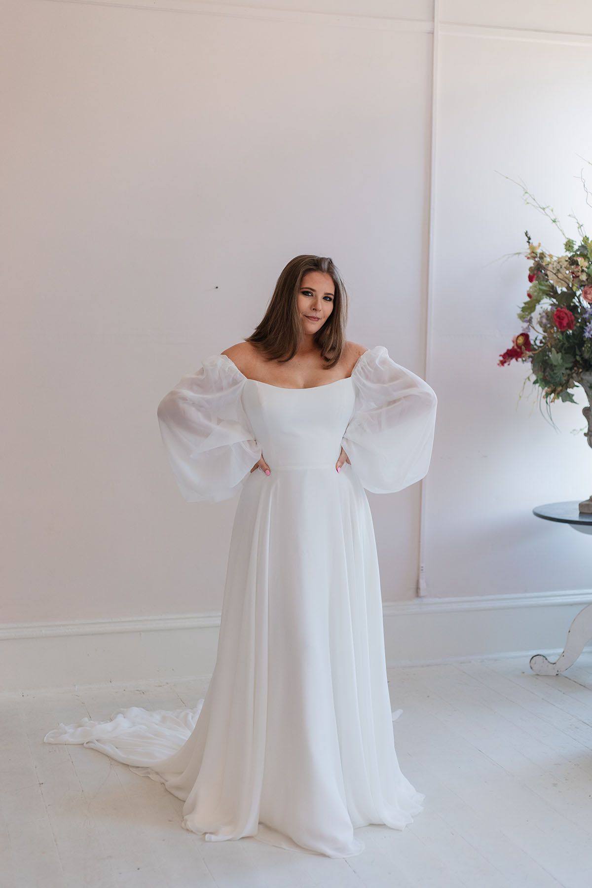 A woman in a white wedding dress is standing in a room next to a vase of flowers.
