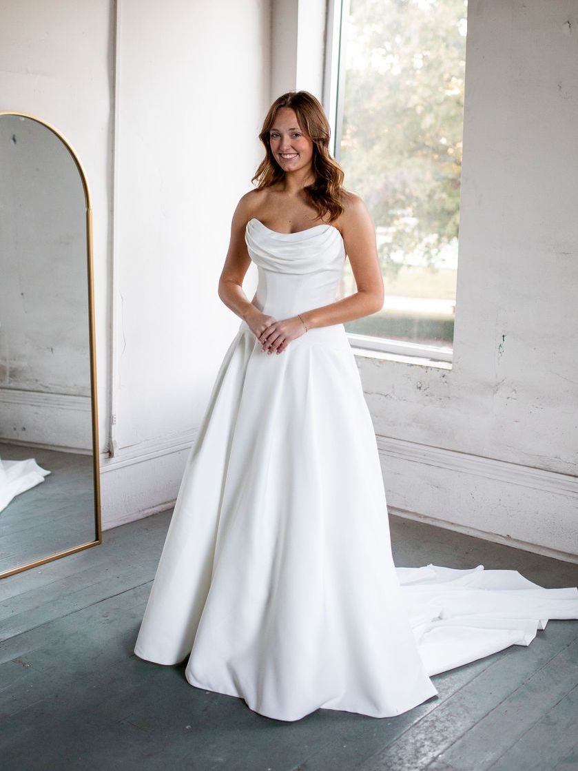 A woman in a white wedding dress is standing in front of a mirror.