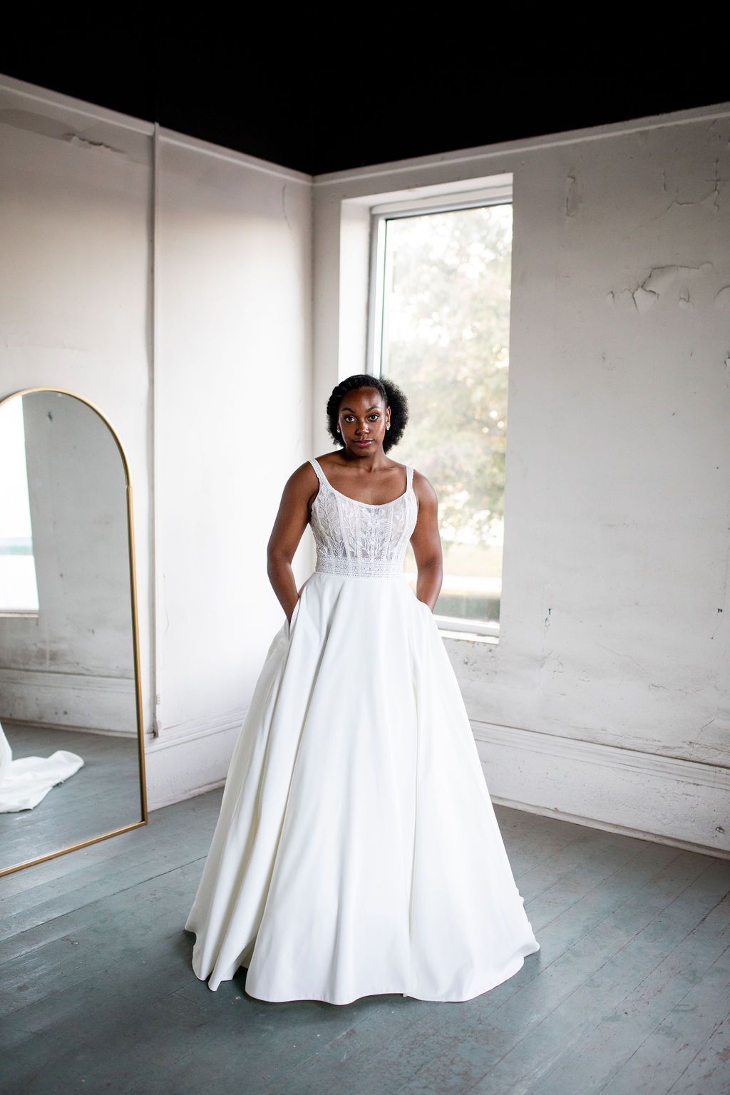 A woman in a white wedding dress is standing in front of a mirror in a room.