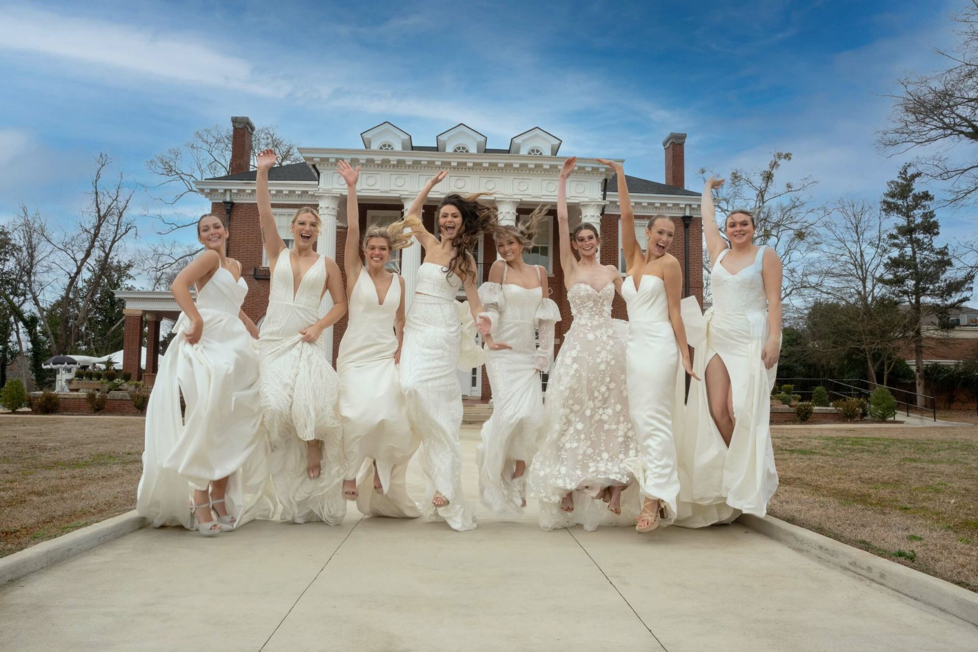 A group of women in white dresses are jumping in the air in front of a building.
