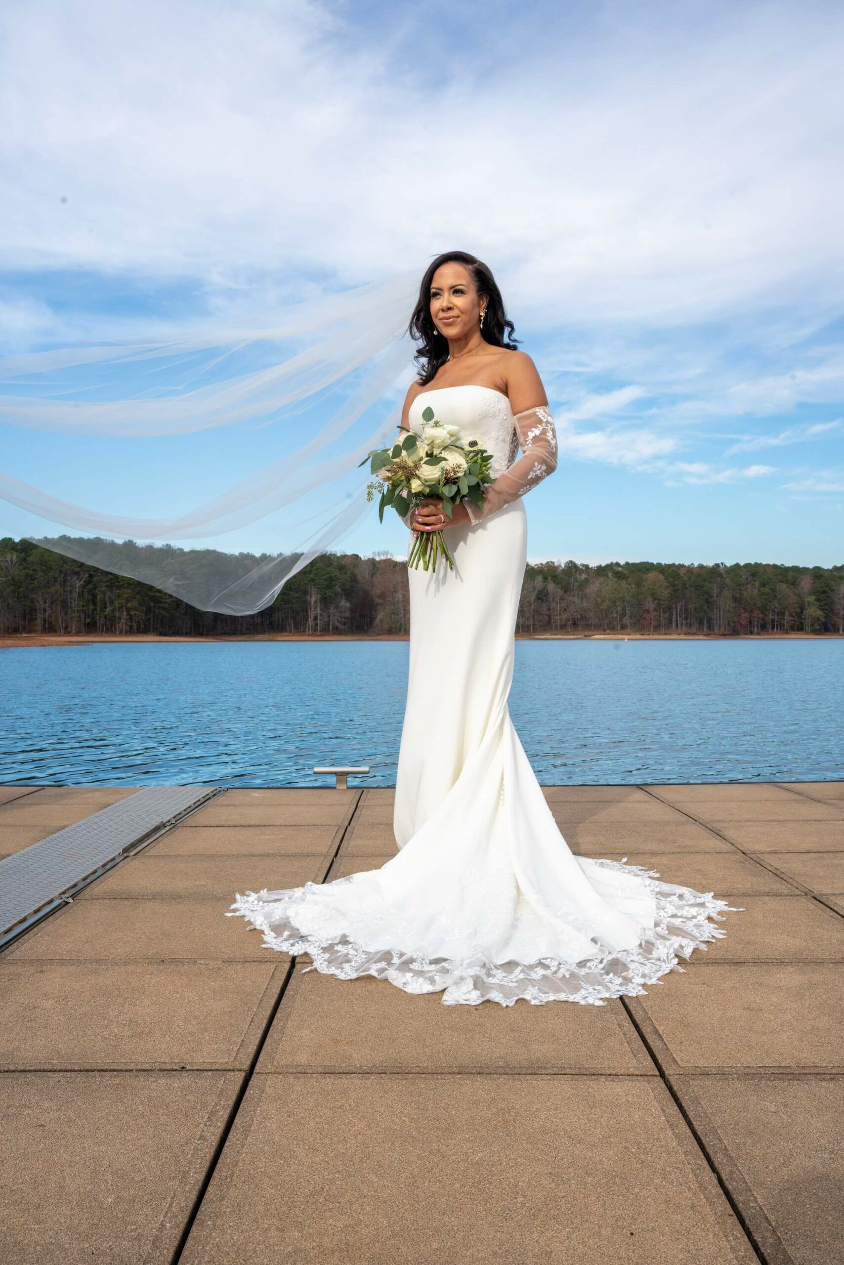 A bride in a wedding dress is standing on a dock holding a bouquet of flowers.