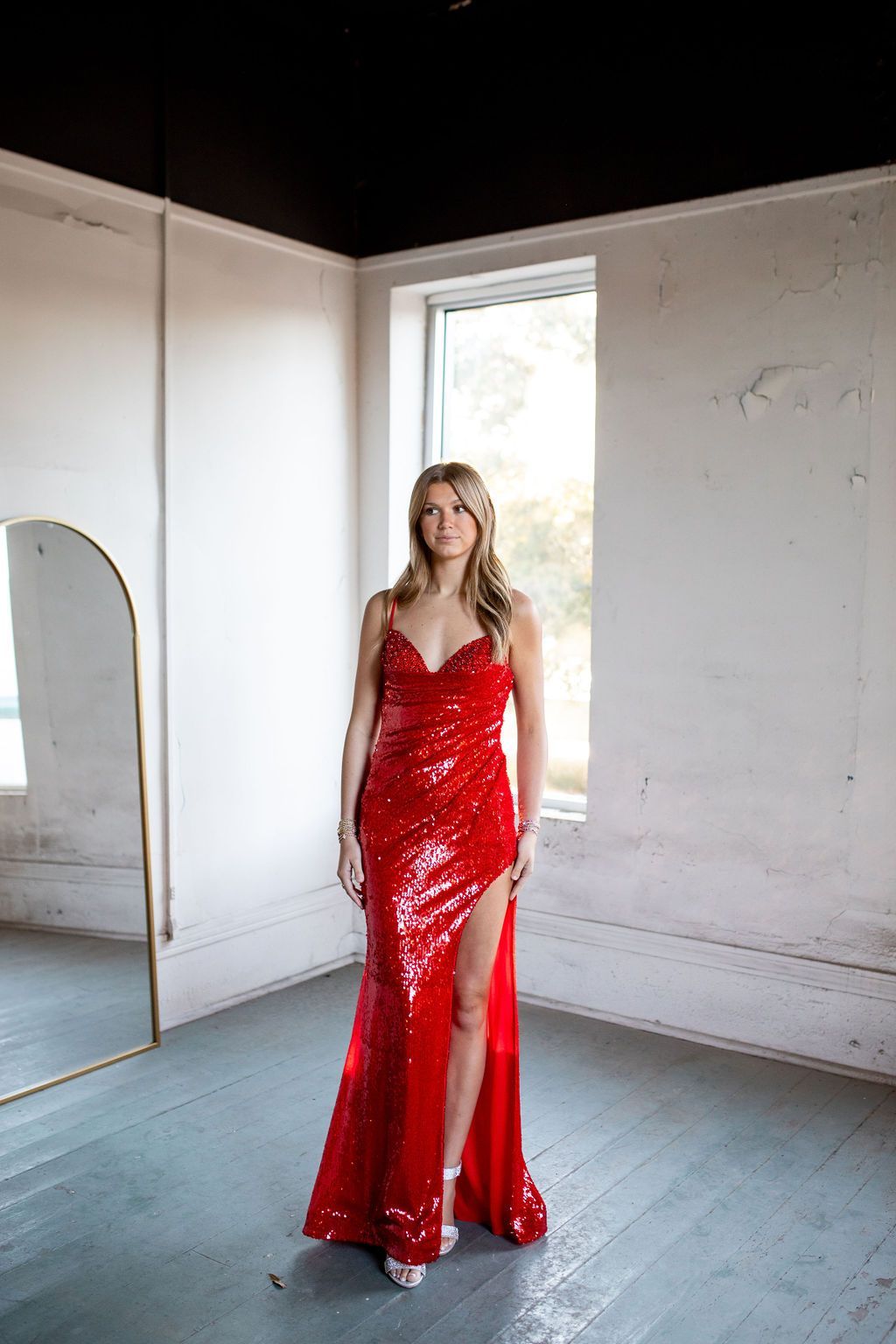 A woman in a red sequined dress is standing in an empty room.