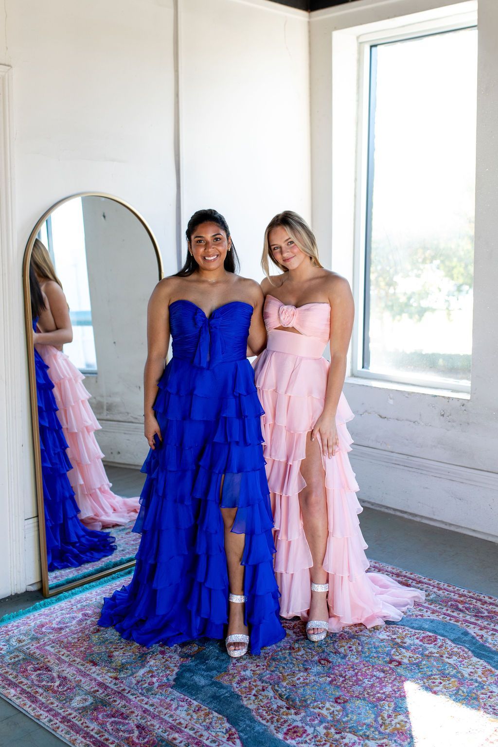 Two women in dresses are standing next to each other in front of a mirror.