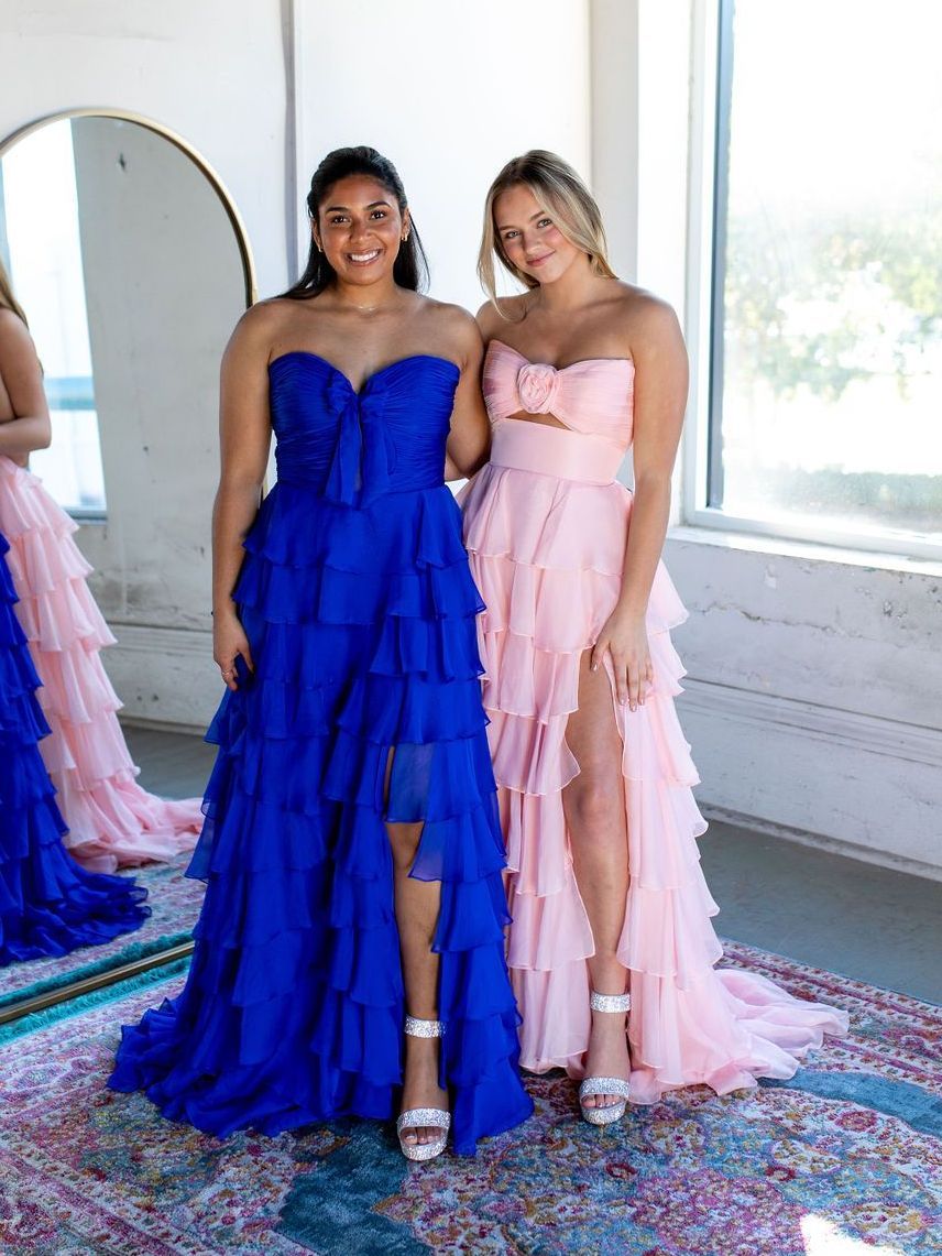 Two women in dresses are standing next to each other in front of a mirror.