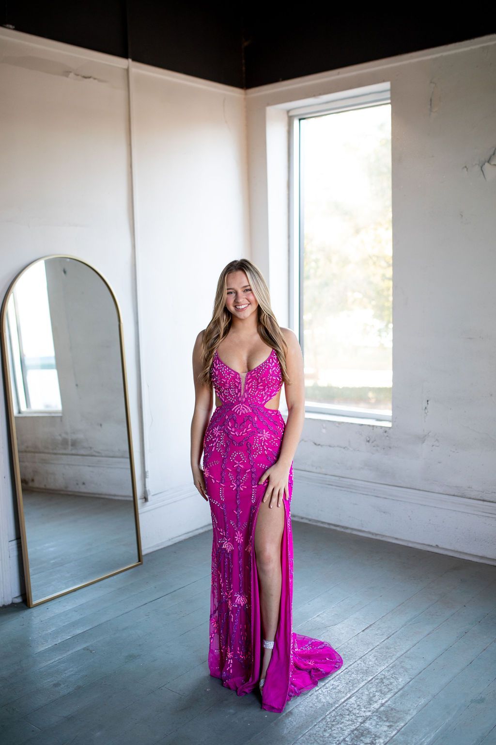 A woman in a pink dress is standing in front of a mirror in a room.