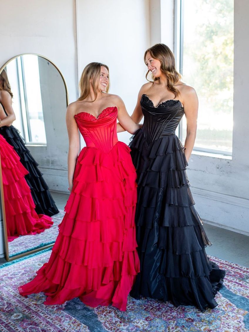 Two women in long dresses are standing next to each other in front of a mirror.