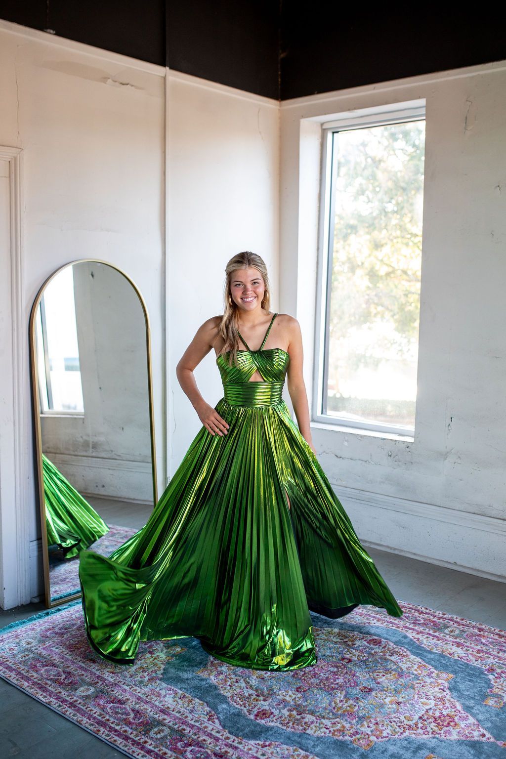 A woman in a green dress is standing in front of a mirror.