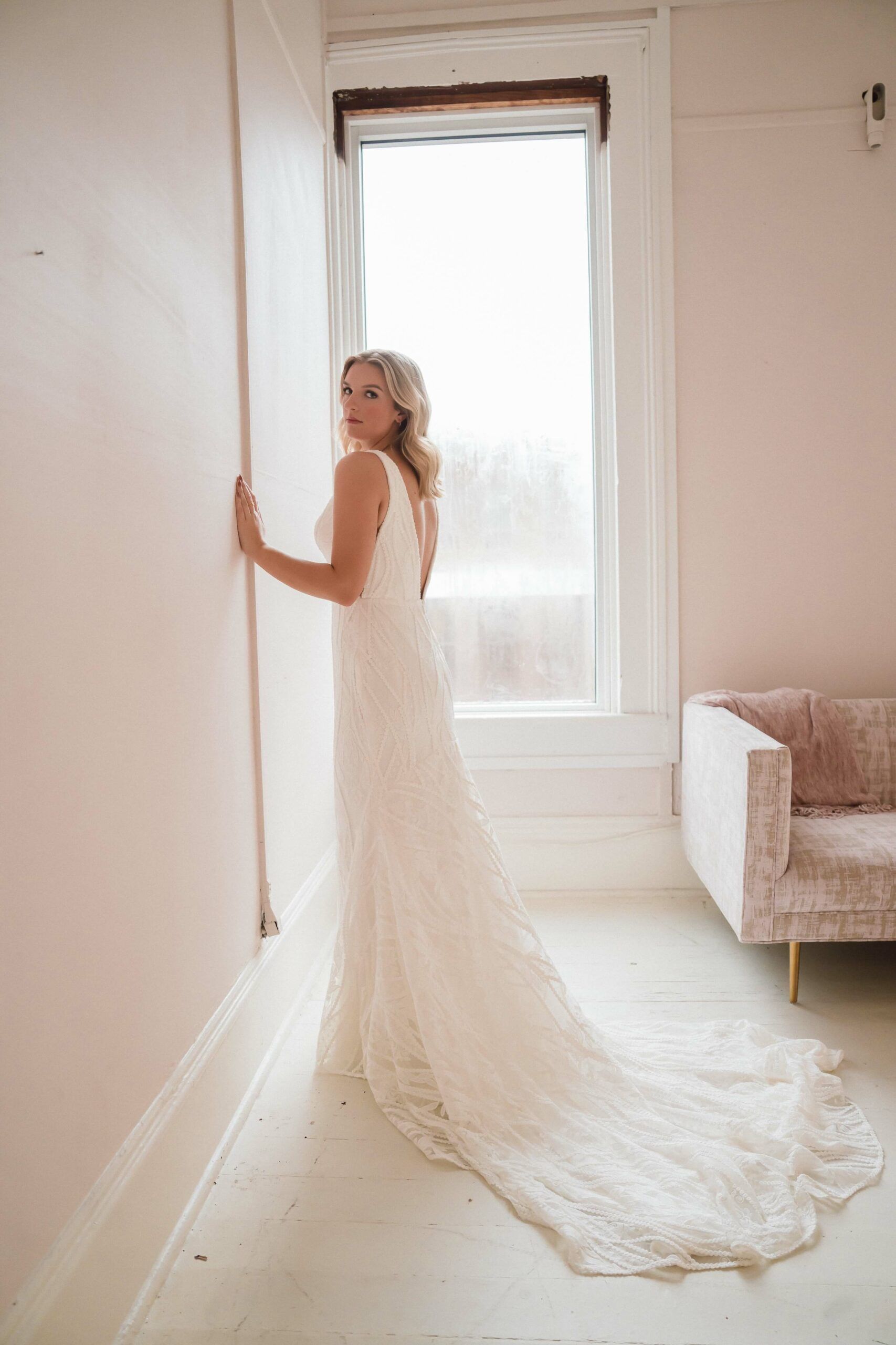 A woman in a wedding dress is leaning against a wall in a room.