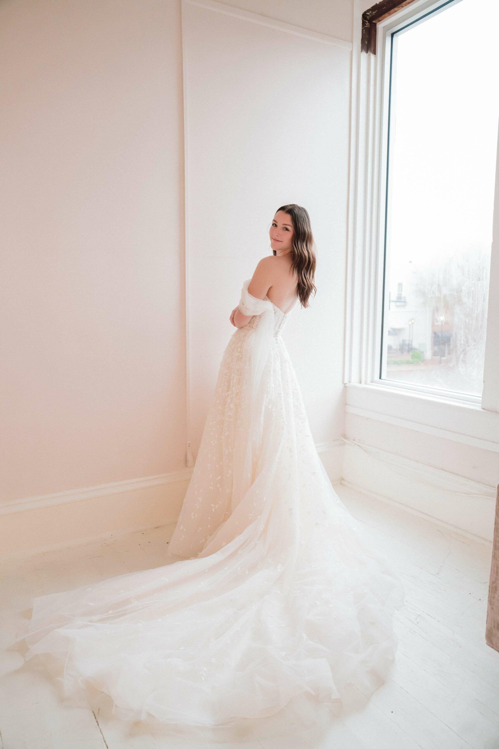 A woman in a wedding dress is standing in front of a window.