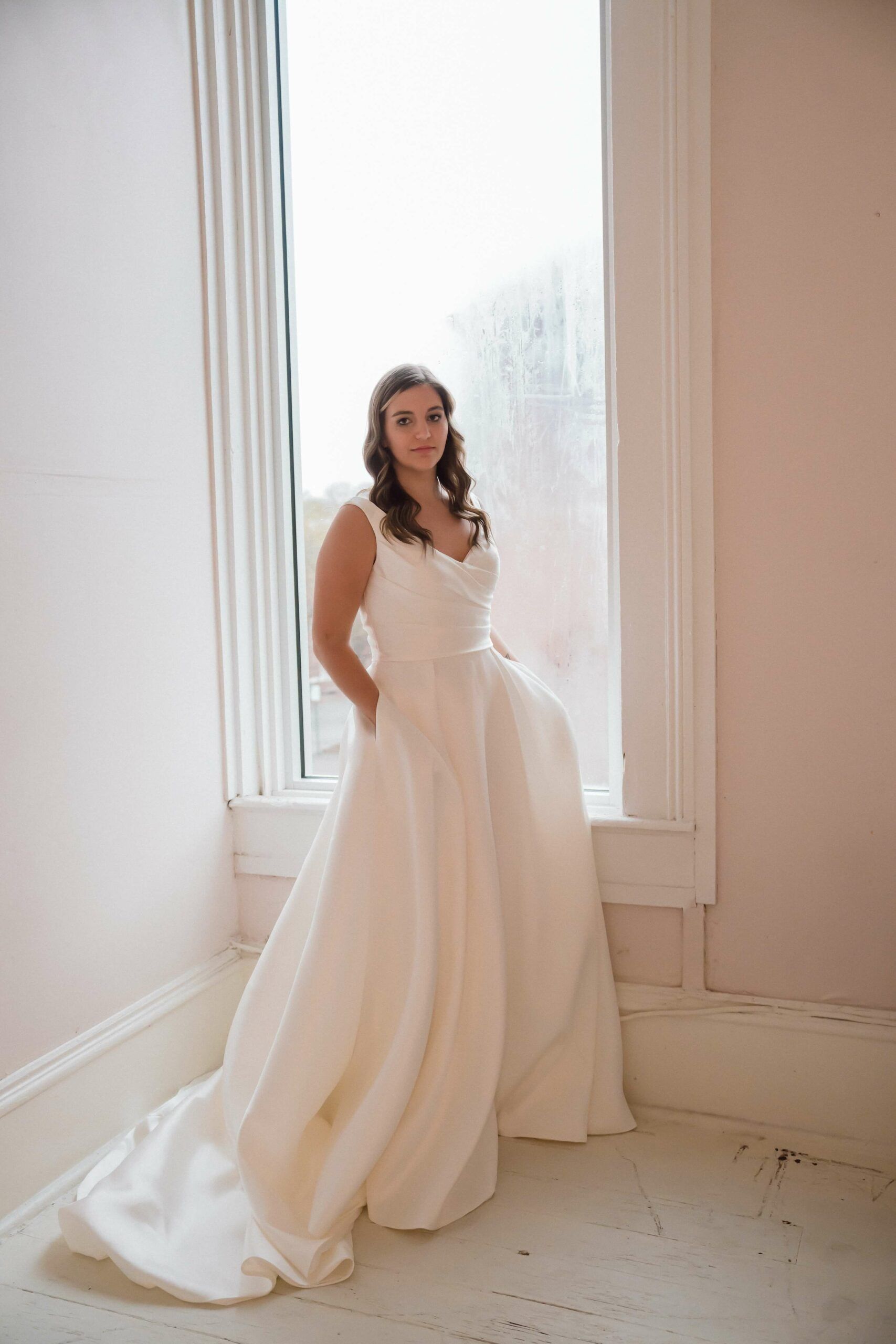 A woman in a wedding dress is standing in front of a window.