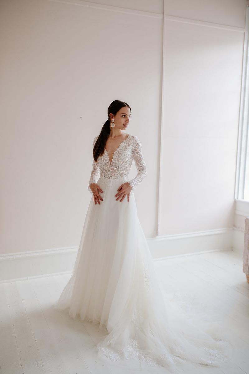 A woman in a white wedding dress is standing in front of a window.