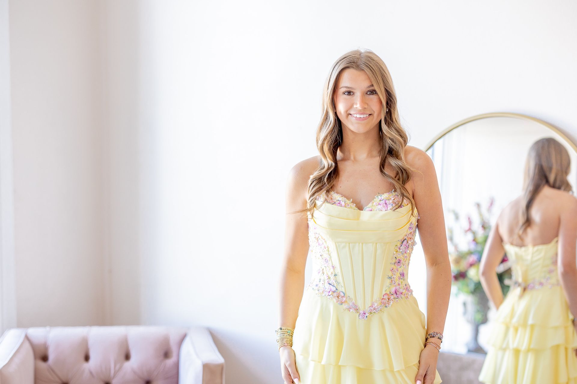 Woman in yellow dress smiles, standing in front of mirror.