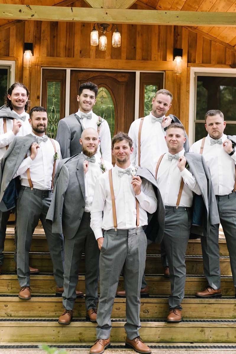 The groom and his groomsmen are posing for a picture in front of a wooden building.