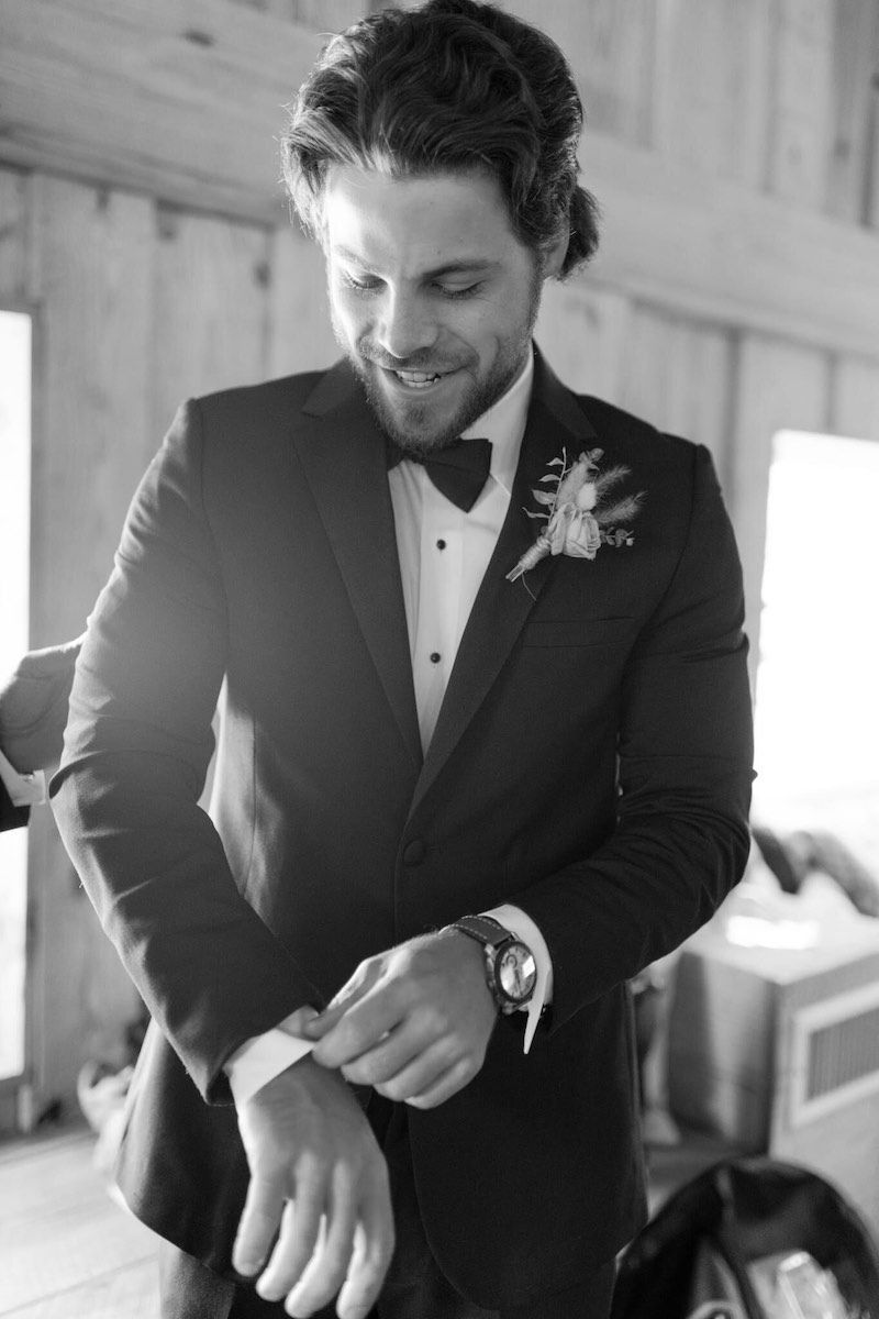 A black and white photo of a man in a tuxedo adjusting his cufflinks.