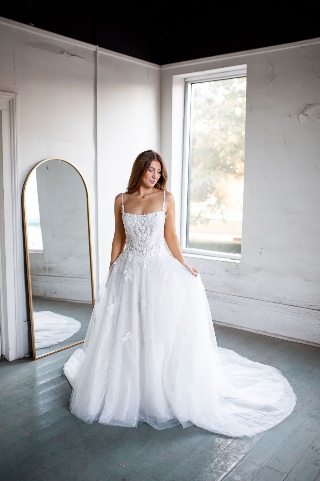 A woman in a wedding dress is standing in front of a mirror in a room.