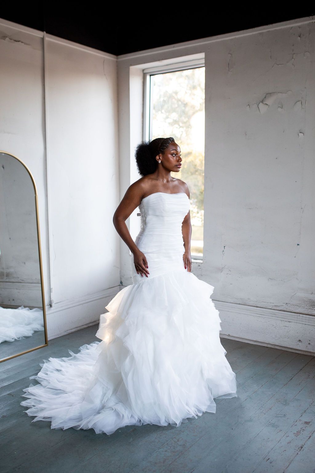 A woman in a wedding dress is standing in front of a mirror in a room.
