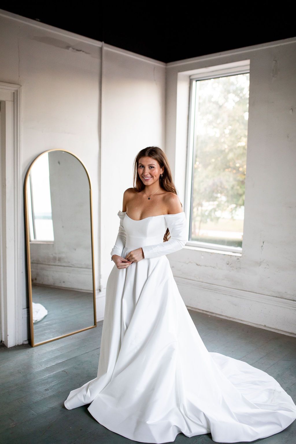 A woman in a white wedding dress is standing in front of a mirror.