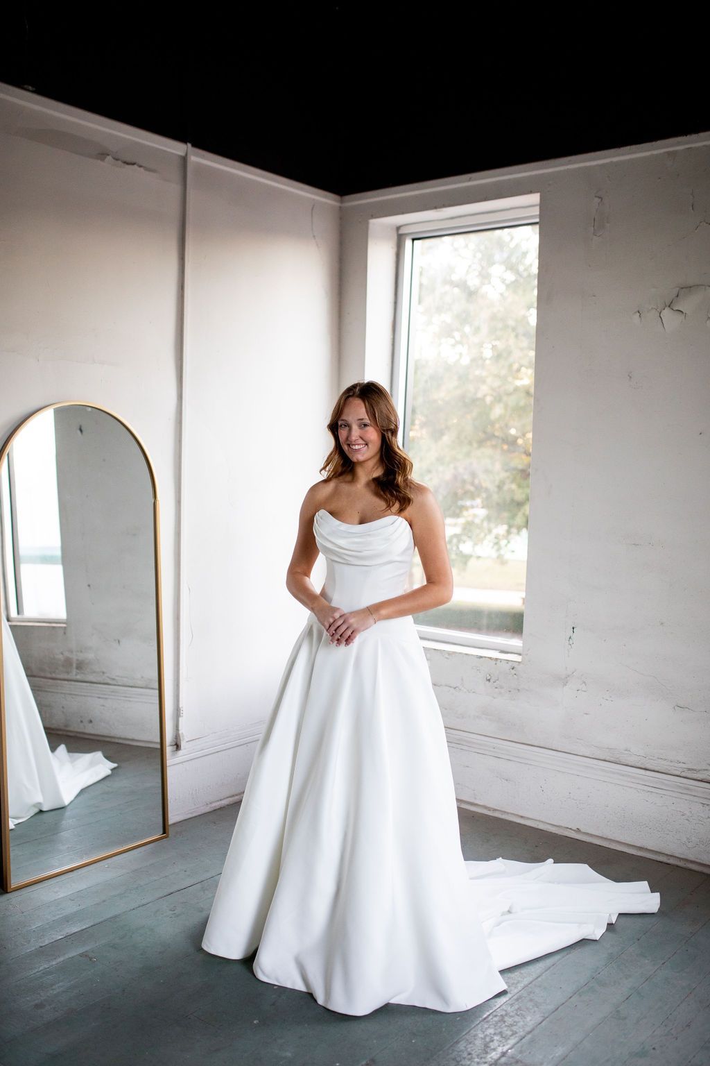 A woman in a white wedding dress is standing in front of a mirror.