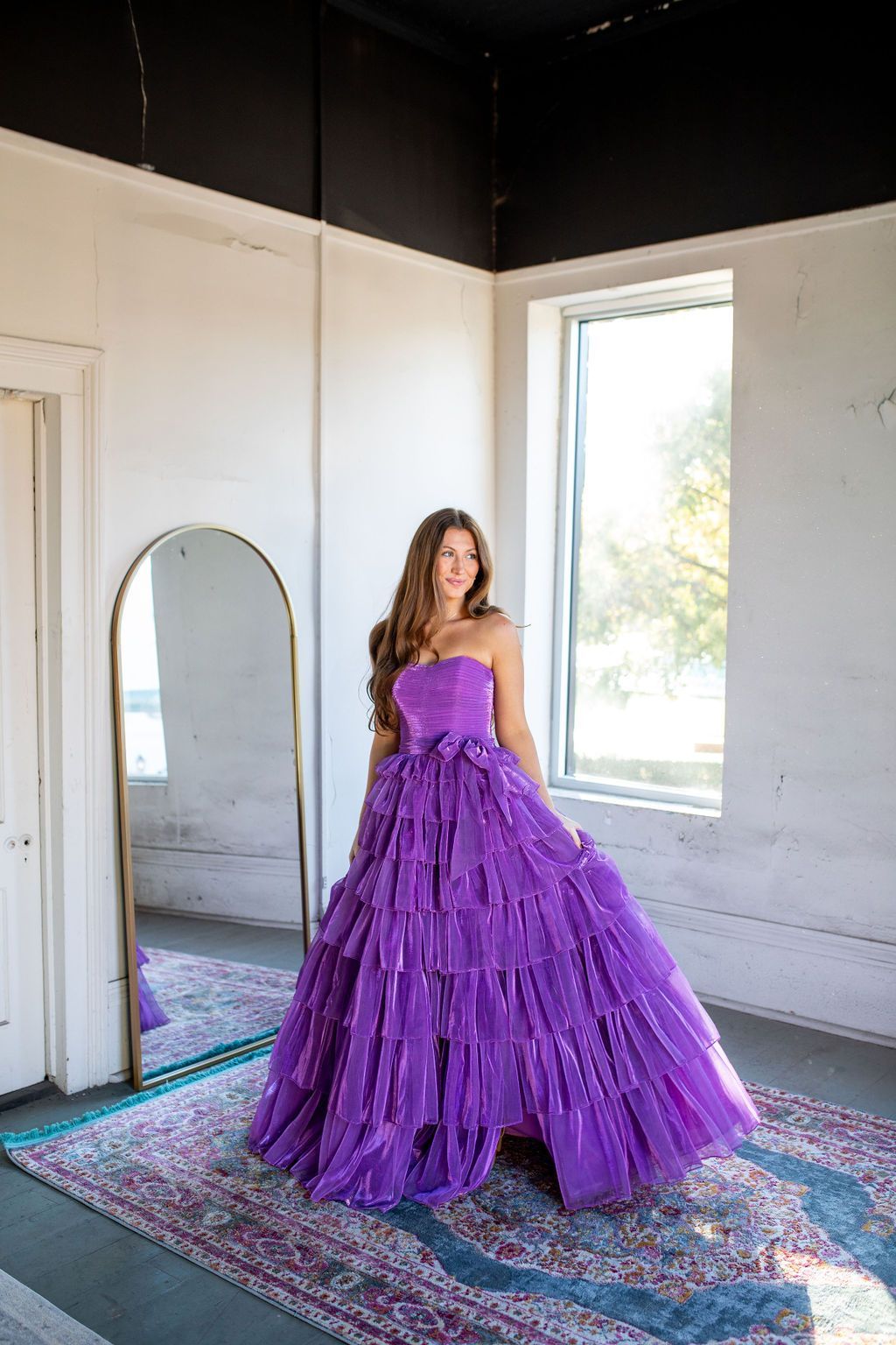 A woman in a purple dress is standing in front of a mirror in a room.