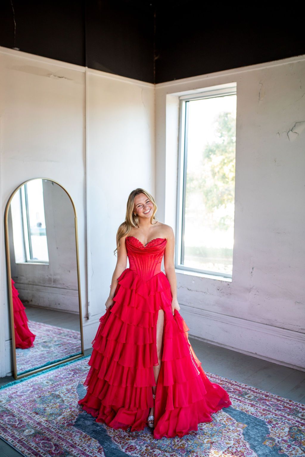 A woman in a red dress is standing in front of a mirror in a room.