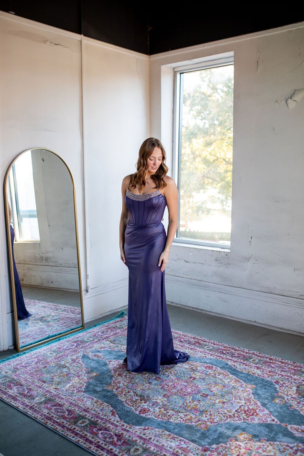 A woman in a purple dress is standing in front of a mirror in a room.