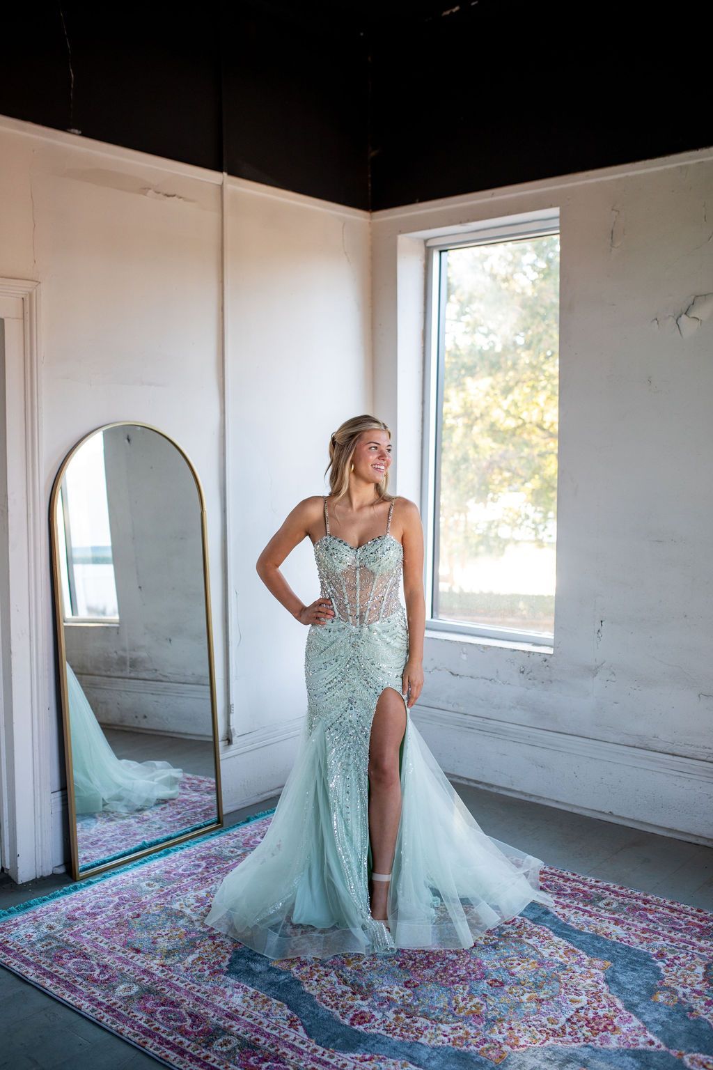 A woman in a dress is standing in front of a mirror in a room.
