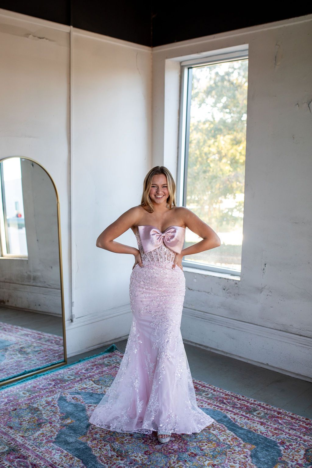 A woman in a pink dress is standing in front of a mirror in a room.