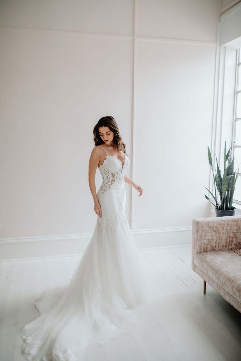 A woman in a wedding dress is standing in a room next to a couch.