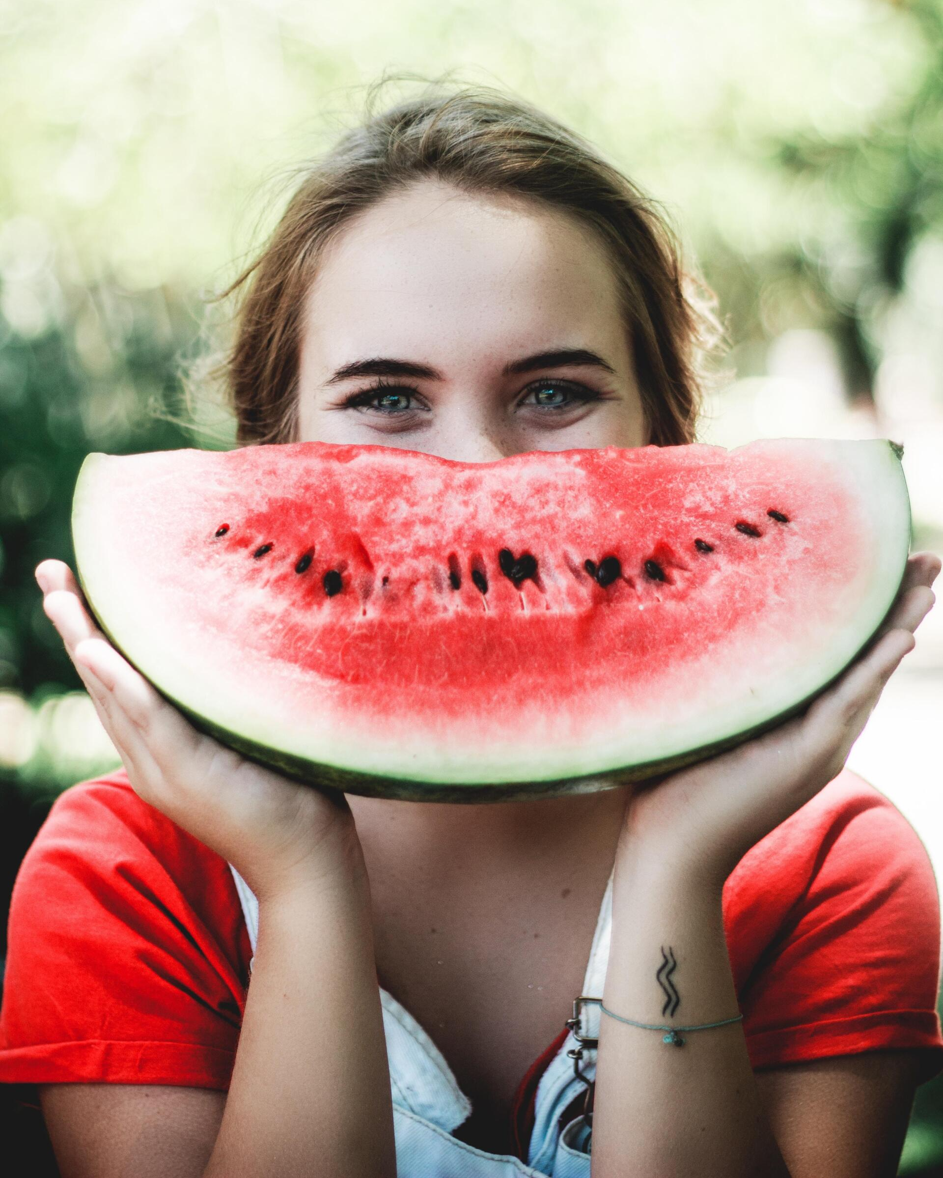 A woman is holding a slice of watermelon in front of her face.