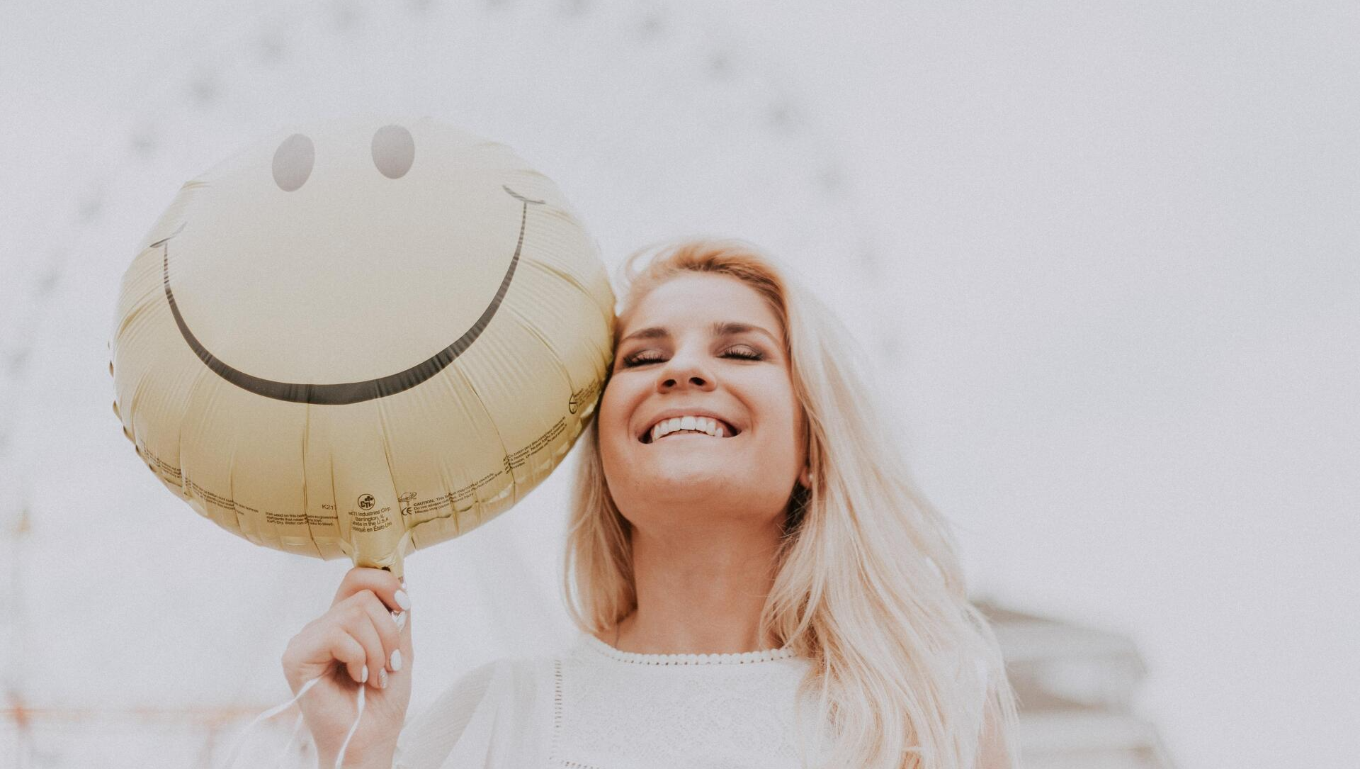 A woman is holding a balloon with a smiley face on it.
