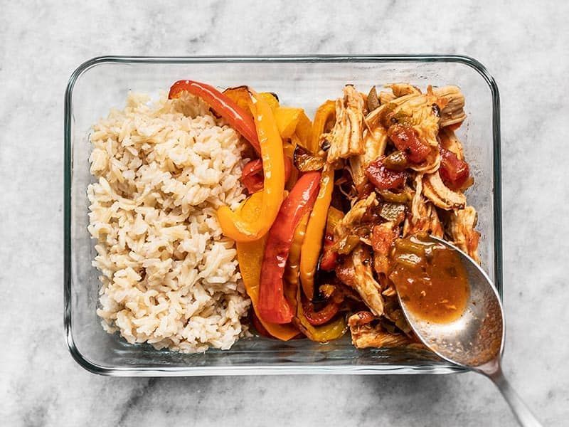 A glass container filled with rice , chicken , and peppers with a spoon in it.