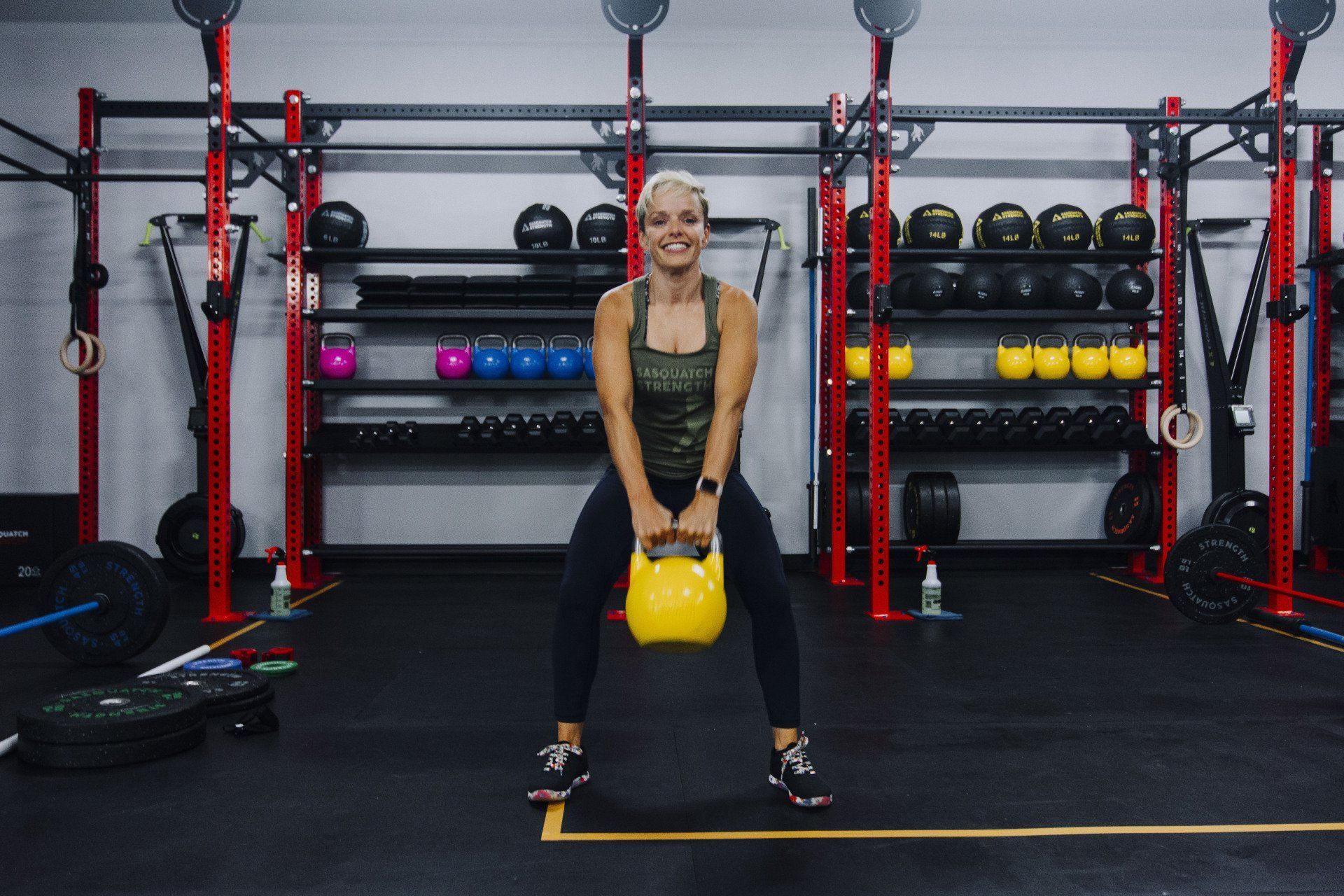 A woman is squatting with a yellow kettlebell in a gym.