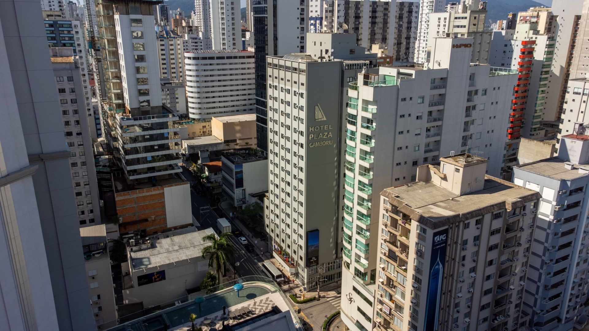 Paisagem urbana com muitos prédios altos. Rua abaixo, com carros e pessoas. Ensolarado, durante o dia.