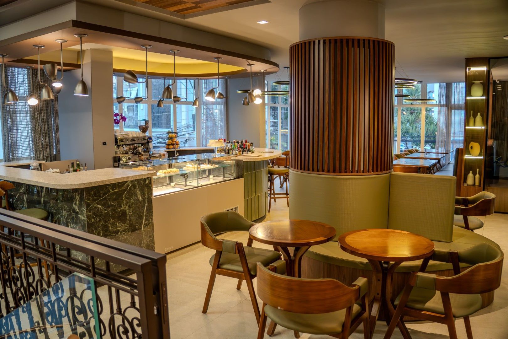 Interior de um café com mesas, um bar e uma vitrine. Cores quentes e luz natural.
