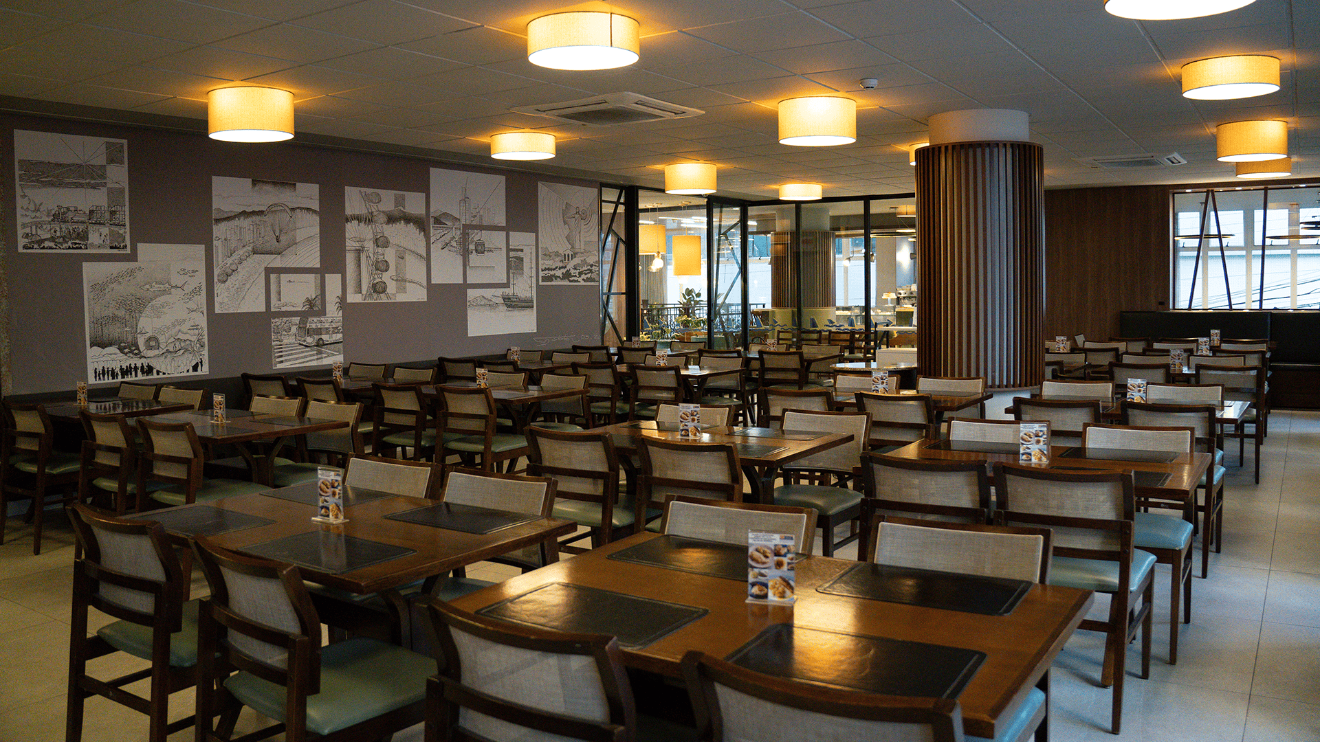 Sala de jantar com mesas e cadeiras, obras de arte na parede e iluminação suspensa.