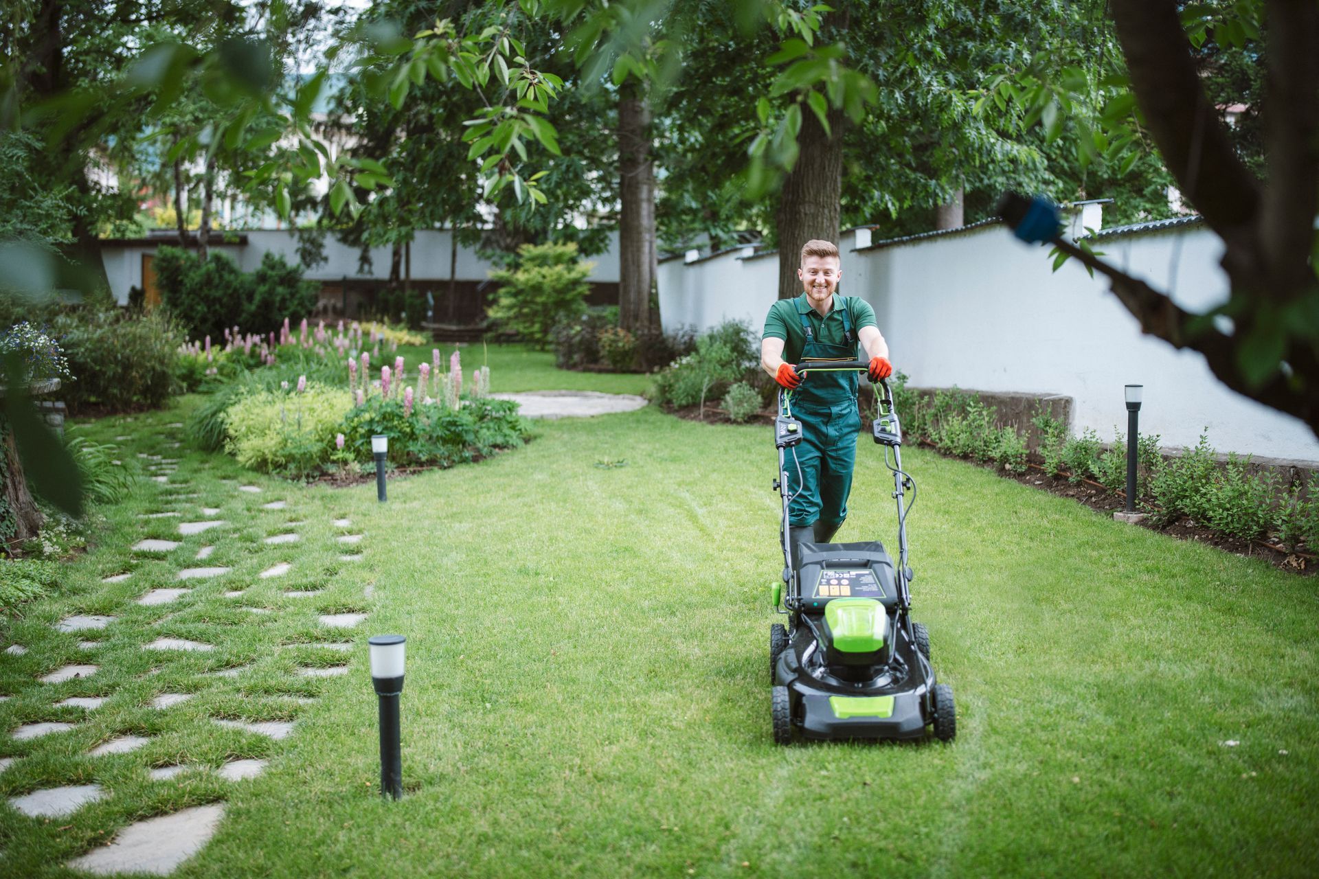 A man is using a green lawn mower to cut the grass in a garden.