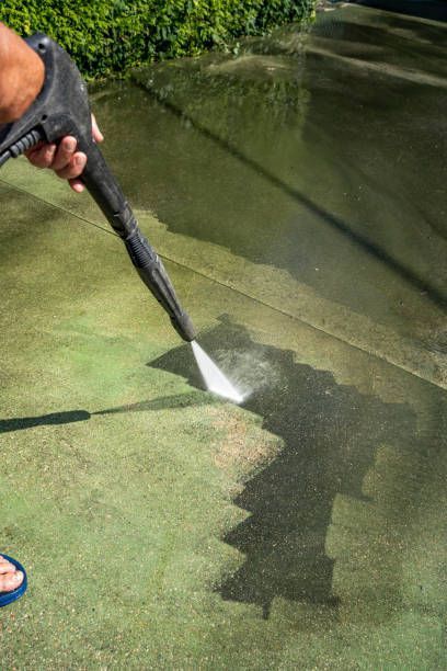 A person is using a high pressure washer to clean a concrete driveway.